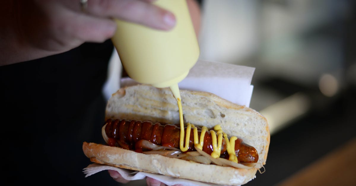 High angle of crop anonymous chef holding delicious hot dog with fried sausage garnished with mustard and ketchup