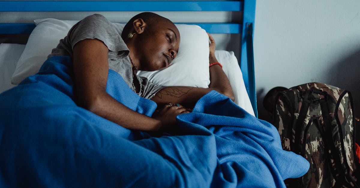 A woman rests peacefully in a hostel bed with a blue blanket and a backpack nearby, conveying travel fatigue.