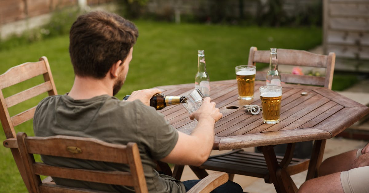 Back view of anonymous male filling glass mug with beer from bottle while chilling with friend at backyard