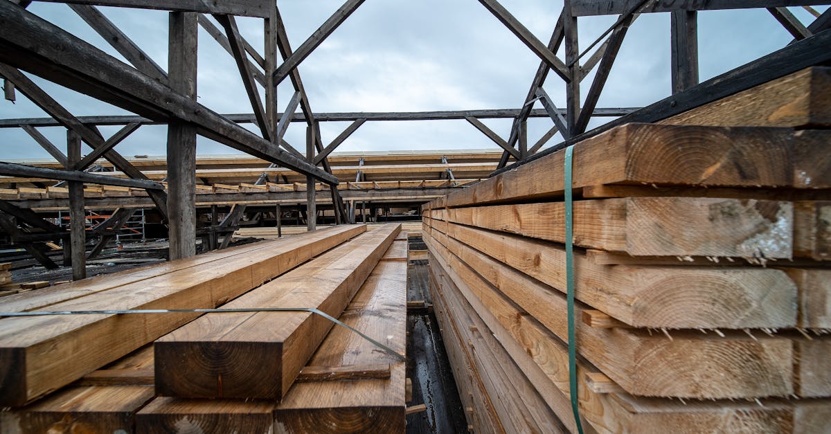 Stacked timber planks in an outdoor industrial storage area under a cloudy sky.
