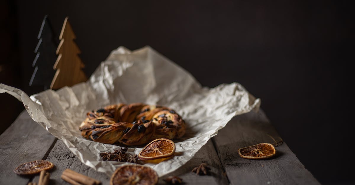 A rustic cinnamon pastry on parchment with dried oranges and spices, captured in moody lighting.