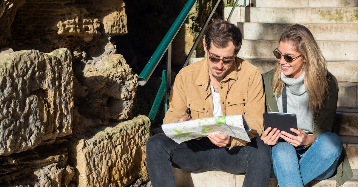 A young couple studies a map and digital tablet on sunny stone steps, planning a travel route.