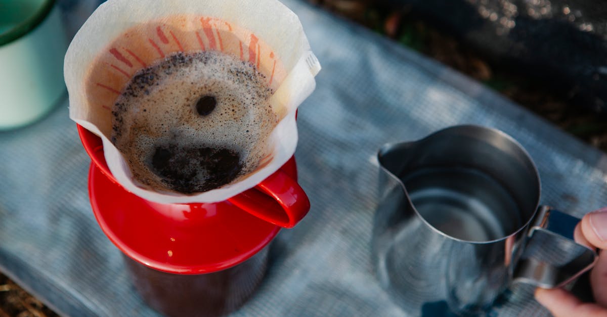 From above of crop anonymous traveler with metal pitcher and freshly brewed coffee in filter in drip coffee maker outdoors