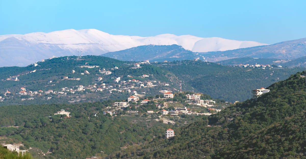 Aerial view of Ghouma village nestled in lush green hills with snow-capped mountains in Lebanon.