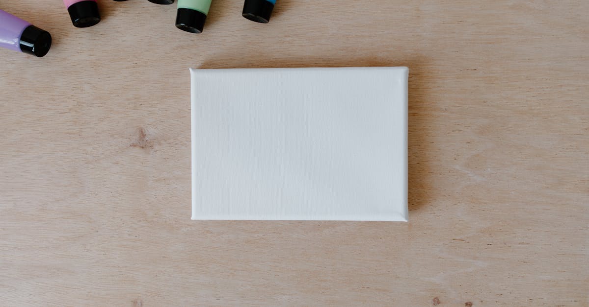 Top view of colorful paint tubes and blank canvas on a wooden surface.