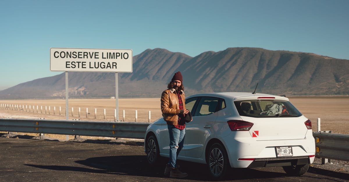 A man beside a white car in a scenic desert landscape with mountains. Sign says 'Conserve Clean This Place'.