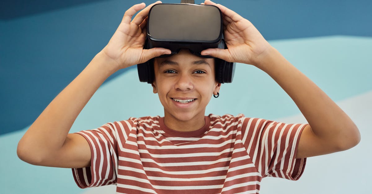 Cheerful little boy in t shirt putting pn VR glasses and looking at camera against blue wall