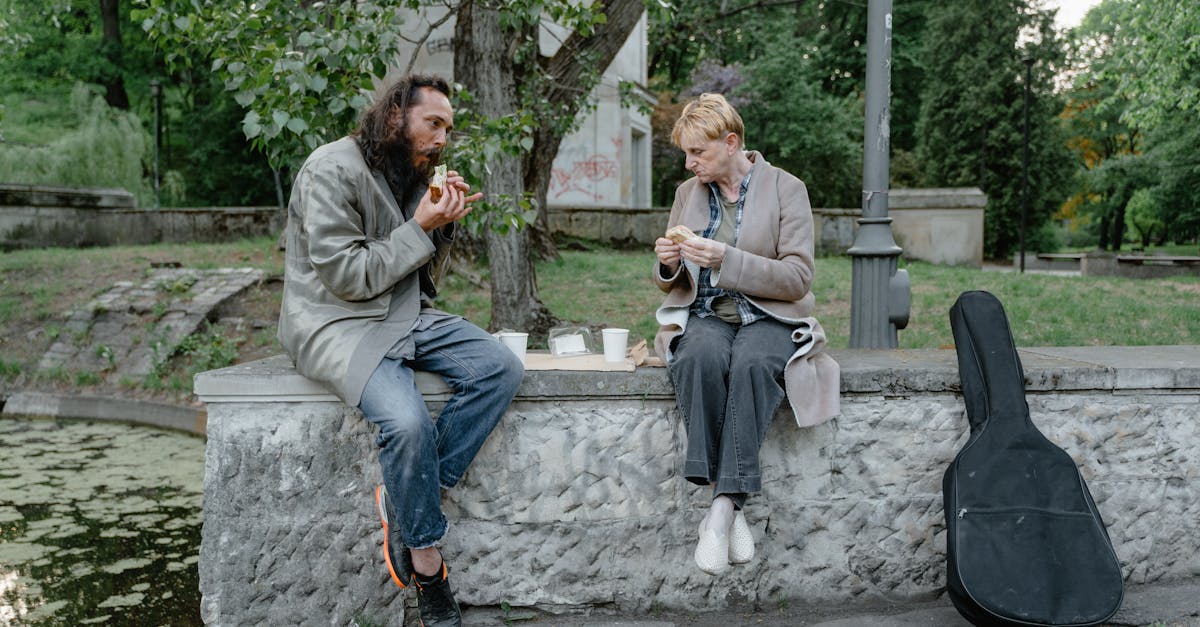 Two individuals sharing a meal outdoors on a stone bench, highlighting companionship and resilience.