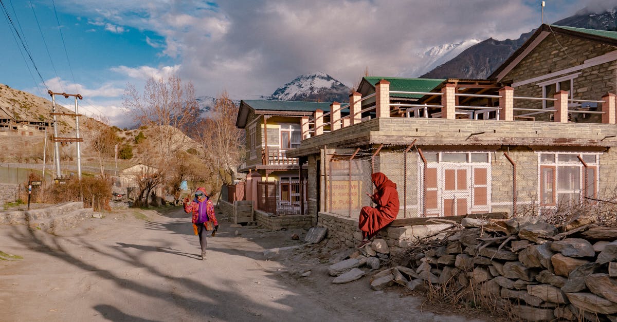 A tranquil village street with a pedestrian and monk, framed by mountains.