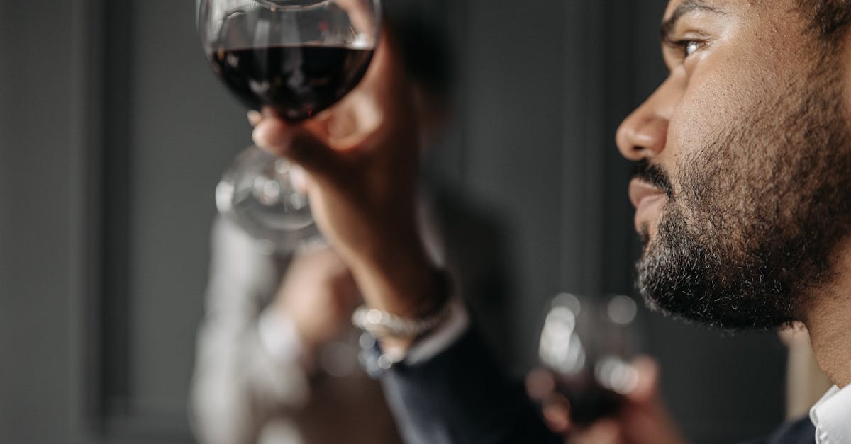 Close-up of a man admiring a glass of red wine indoors, showcasing a moment of elegance.