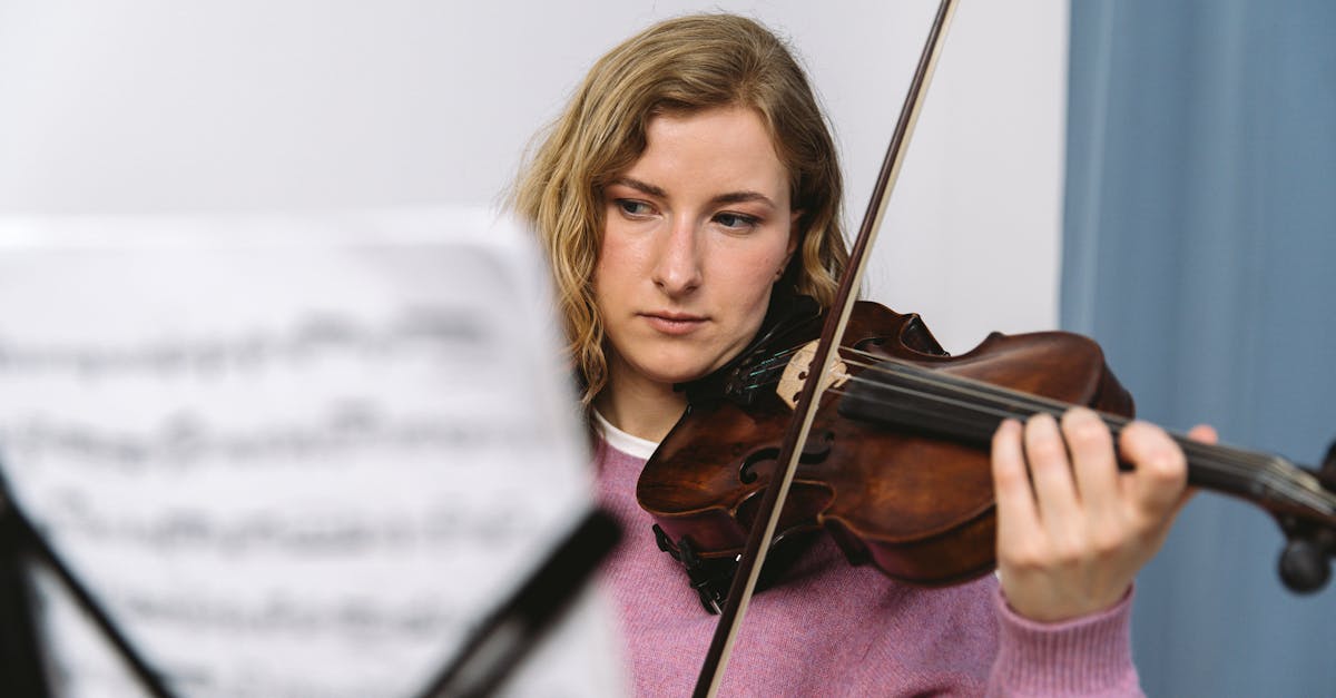A focused young woman playing the violin, reading sheet music indoors.
