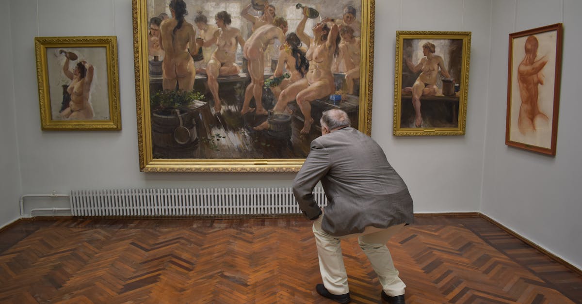 A man closely examines paintings in an art gallery, featuring nude art.