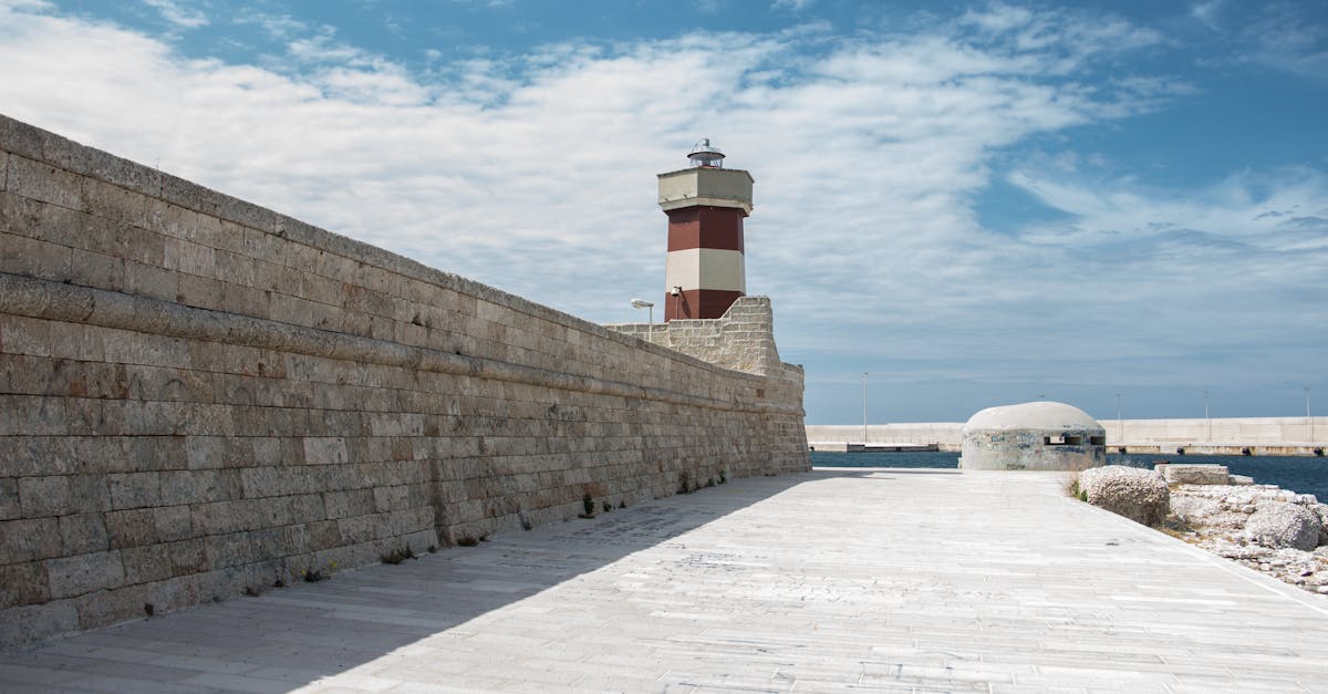 A picturesque lighthouse by the seashore with a stone wall and blue sky, perfect for travel or architecture themes.