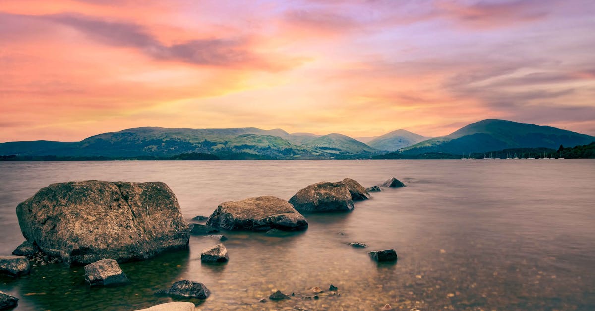 Peaceful sunset view over Loch Lomond with rocky shoreline and distant hills in Scotland.