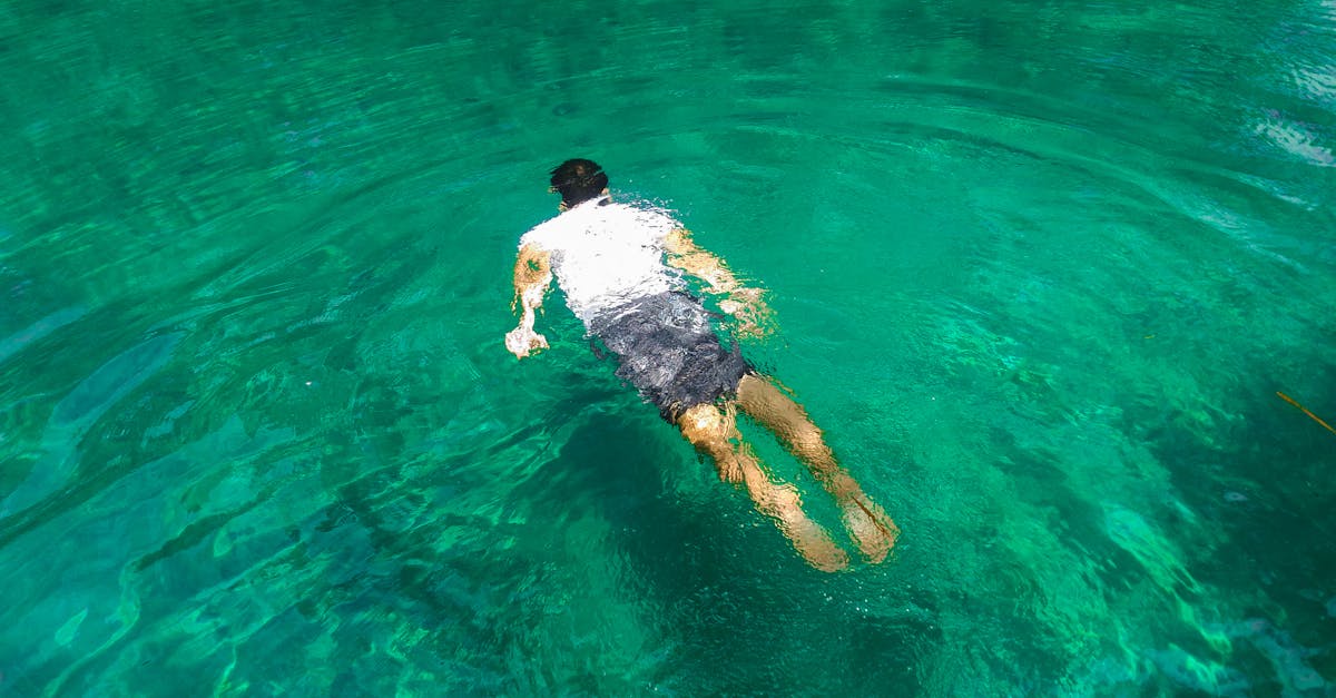 A man swims underwater in clear, vibrant green-blue tropical waters, enjoying leisure time.