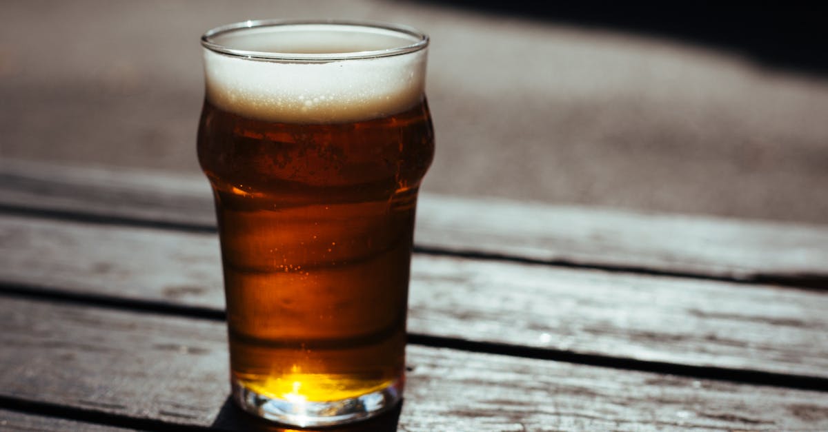 A cold pint of beer on a wooden table in a sunny outdoor setting, perfect for a summer day.